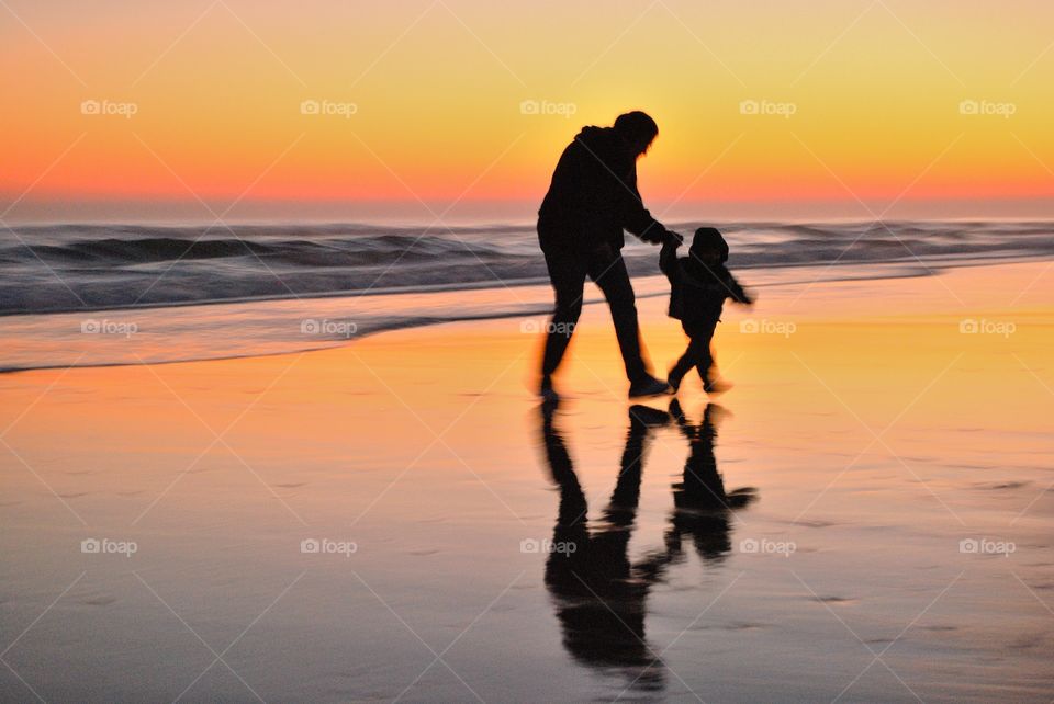 Woman holding the hand of a child running from waves 