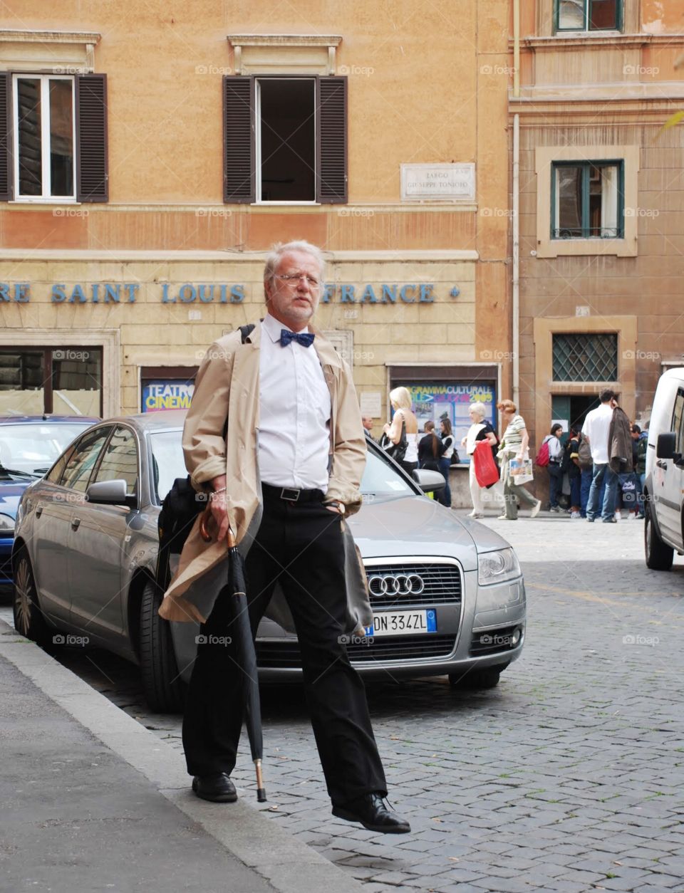 Jaunty Gent. A gentleman decked out in a bow tie and a classy walking stick walks in front of an Audi in Rome