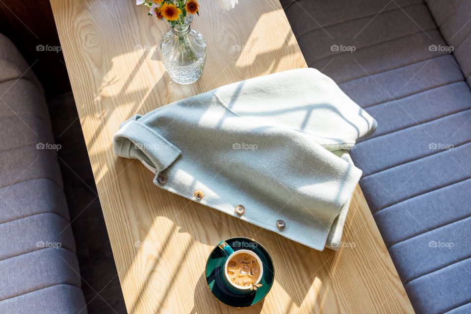 Trendy green coat lying on table in cafe