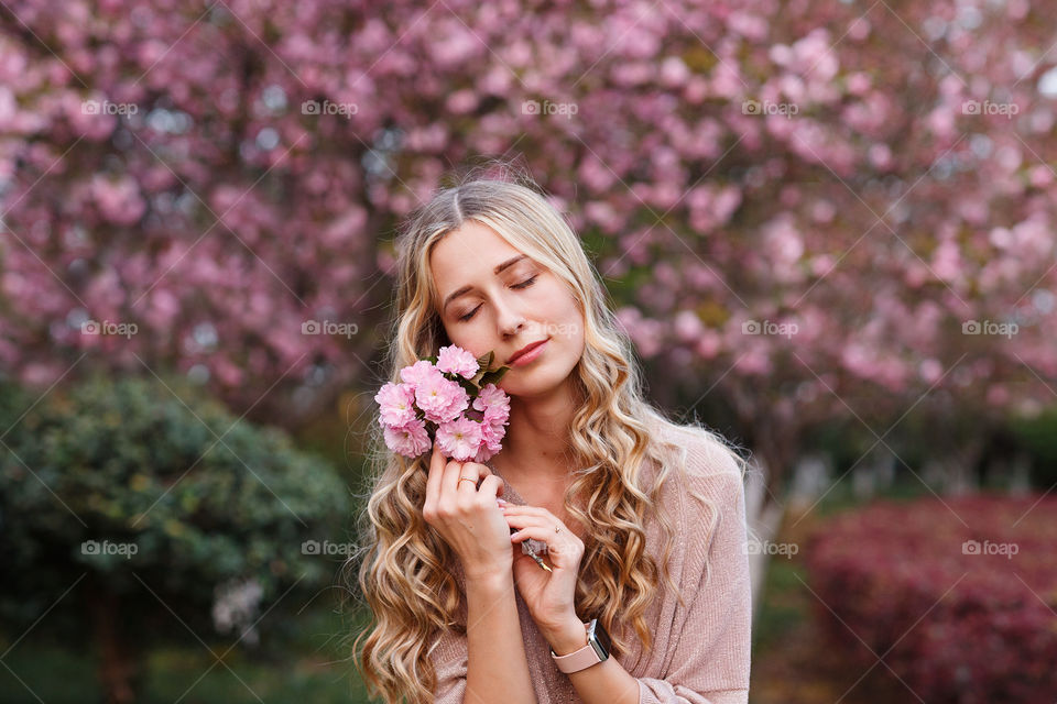 Portrait of beautiful Caucasian woman with blonde hair and closed eyes in blooming park 