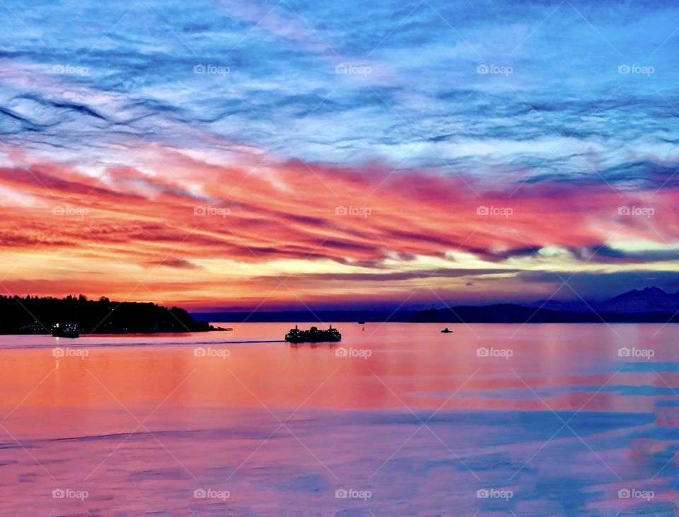 Ferry boat sails across red ocean under setting sun