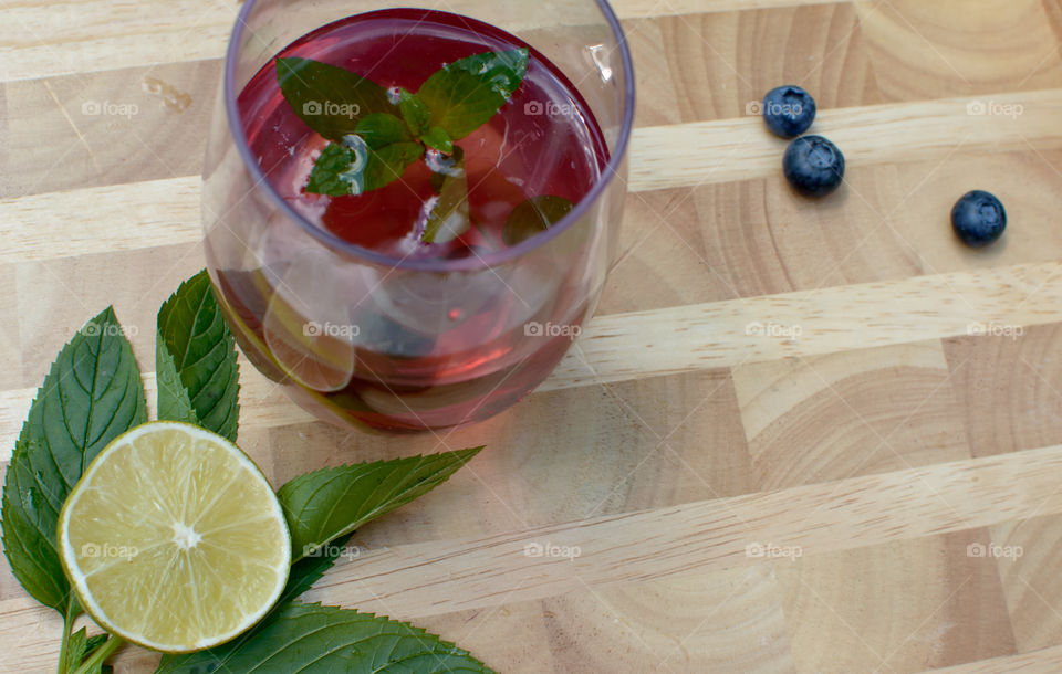 High angle view of beautiful homemade blueberry, lime and mint  flavored water or juice with fresh ingredients on wood table with sliced cross section of lime 