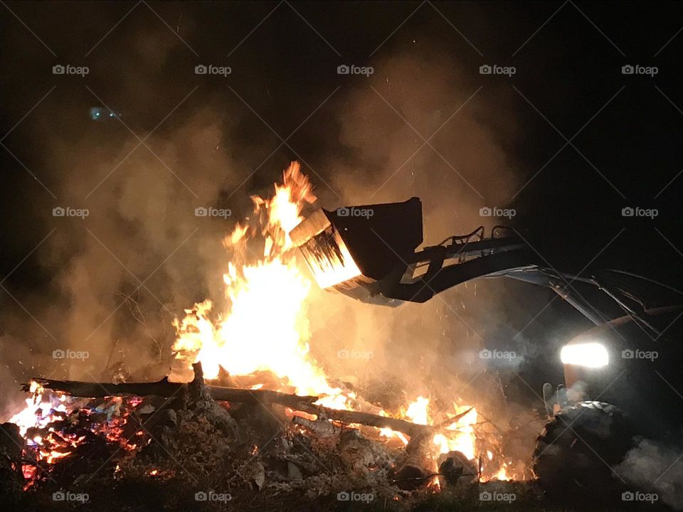 Large bonfire with front loader adding firewood at night. 