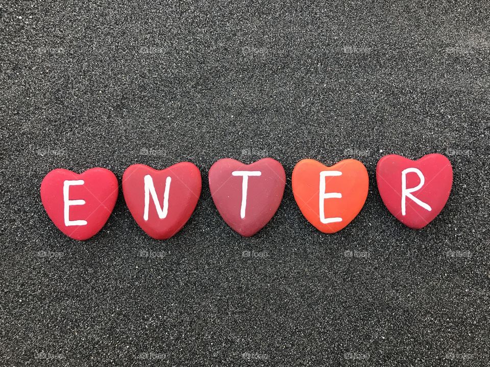 Enter word with colored heart stones over black volcanic sand 