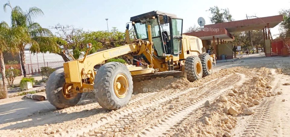 Lateral view of a grader machine, with triple tires. Look at the blade scraping the sad