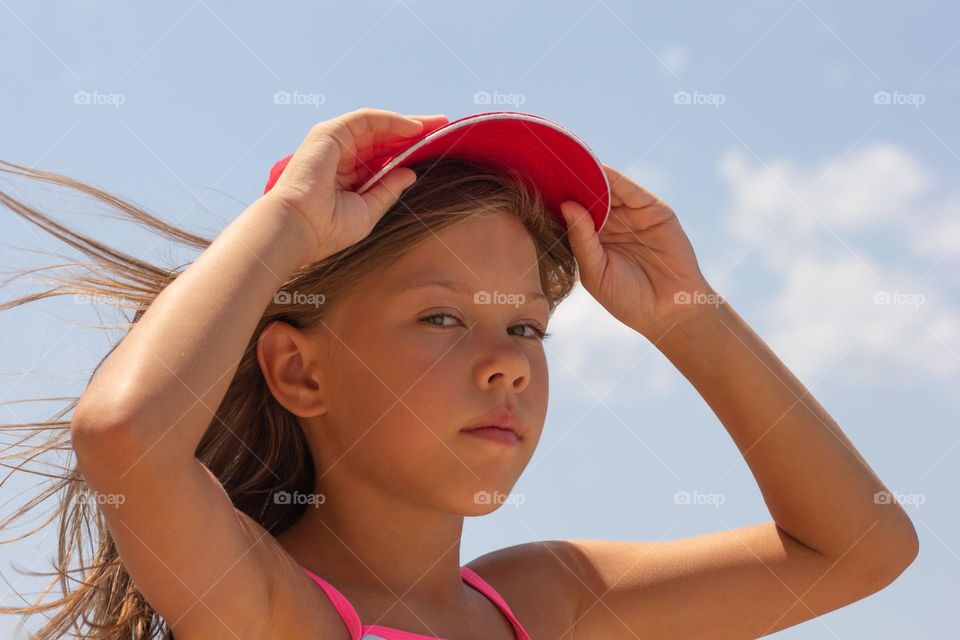 Beautiful caucasian child of 7-8 years putting on baseball cap on sky background