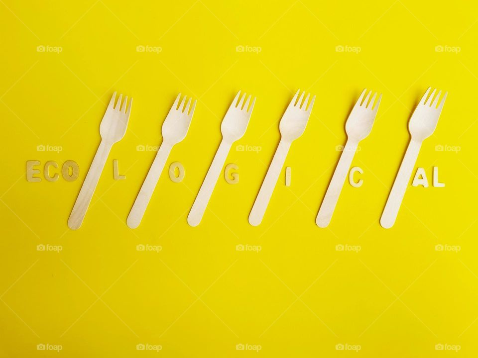 eco wooden cutlery placed on a yellow background with ecological inscription