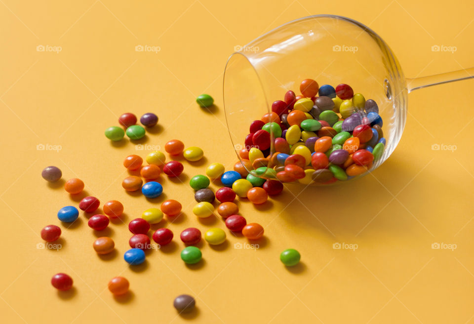 Sweet colorful candies and a glass on yellow background