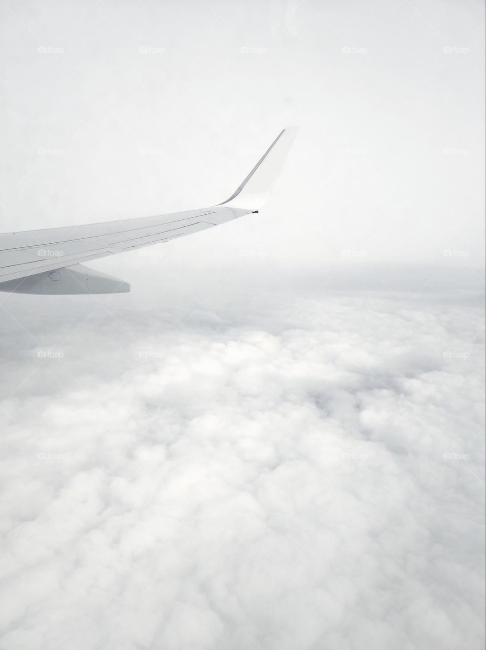 An all-white photo of an airplane in the clouds with its wing visible and beautiful white clouds looking like cotton candy