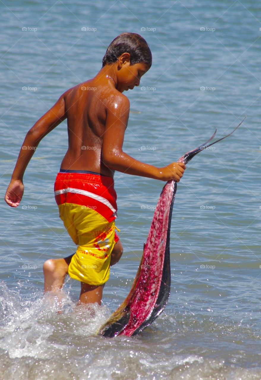 Exterior daylight.  La Peñita de Halteba.   A boy takes a mahi-mahi fish carcass to a boat.  