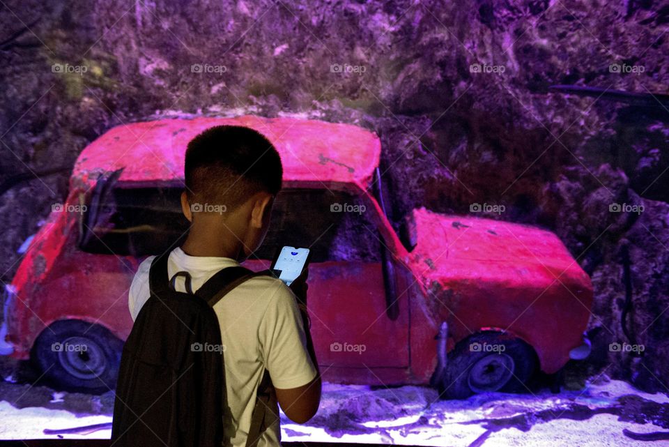 A boy with a backpack and a phone examines an exhibit in an aquarium