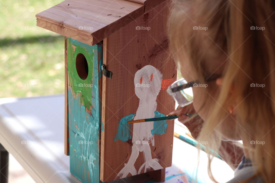 Child painting a wooden bird house