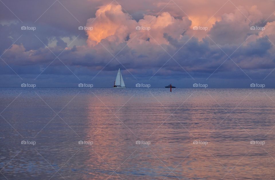 white sailboat on the dramatic sky background during august sunset at the baltic sea in poland