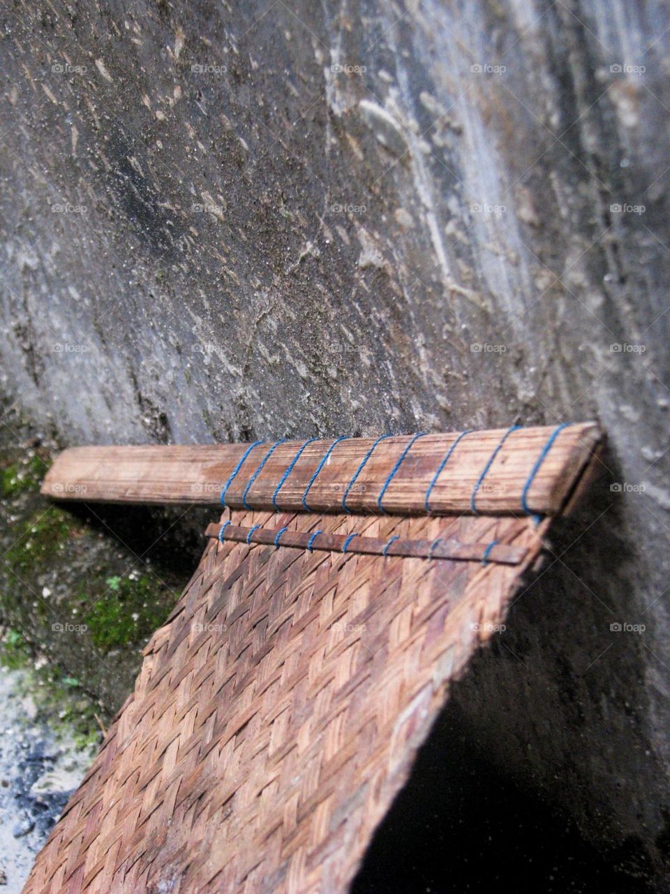 Close-up view of a dull and old woven bamboo fan next to a dull wall