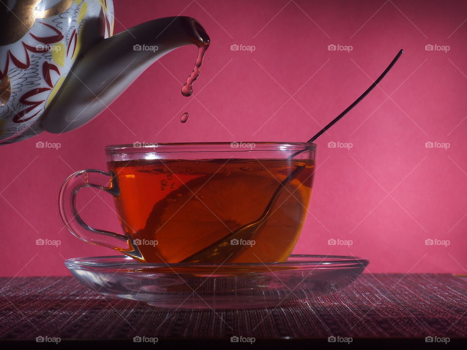 Tea from a teapot is poured into a transparent glass cup.  Tea with lemon in a cup.