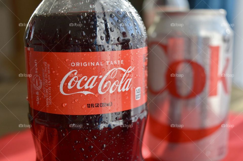 A plastic bottle of Coca-Cola with condensation drops and a can of diet Coca-Cola in the background