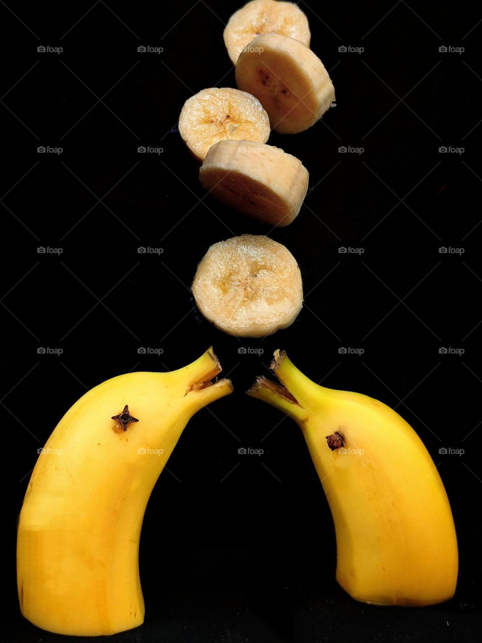 Fruit. Edible still life. Two parts of yellow bananas in the form of dolphins with open mouths look at mugs of cut bananas that fall from above. Background black