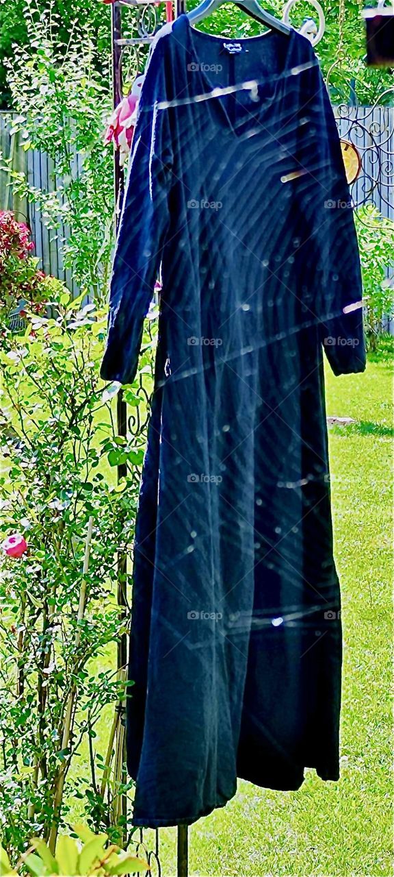 This dark undergarment hung out in the sun to dry was photographed through the unique multifaceted pattern of a large spiderweb which lends this image of a beautiful garden in „Lower Bavaria“, Germany a special flair. 2024. Hypnotic Productions