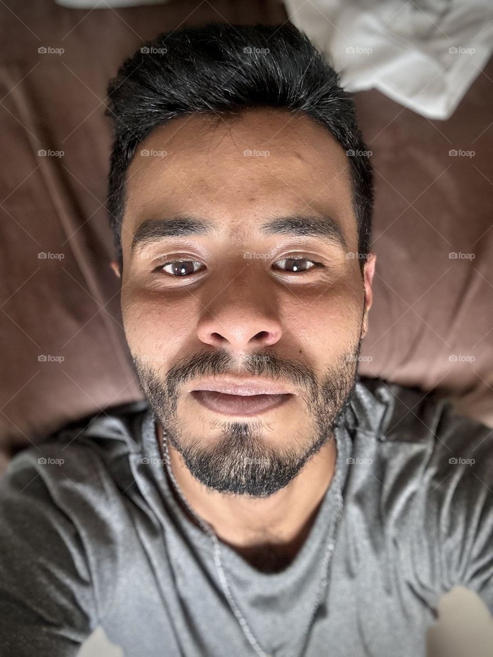 Man lying down on his bed while he looks to the camera and looking thoughtful at his eyes.