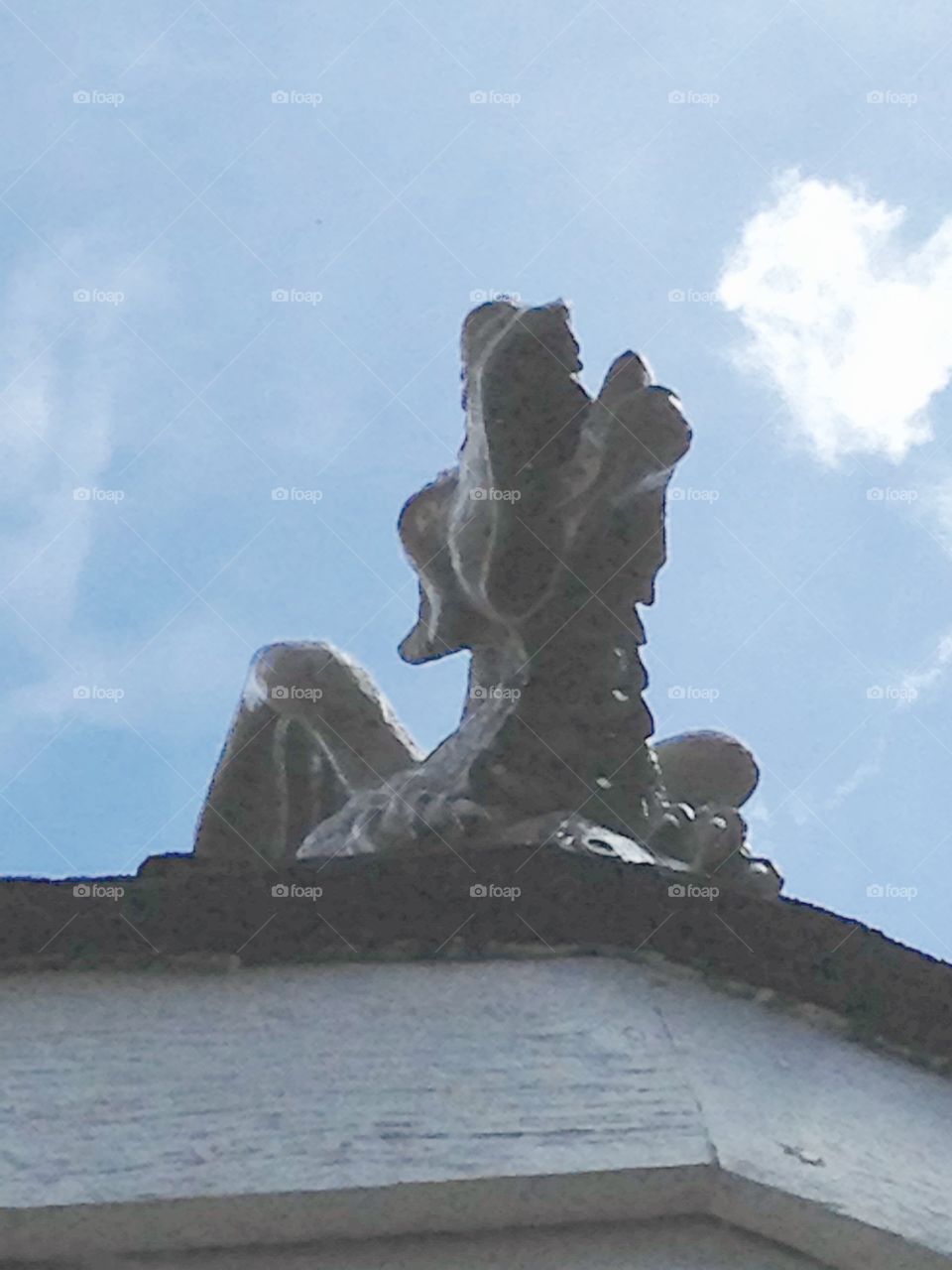 Dragon Gargoyle Roaring. Looking Up we have a Dragon Gargoyle atop a peak overlooking our yard. The sky is blue with white clouds.