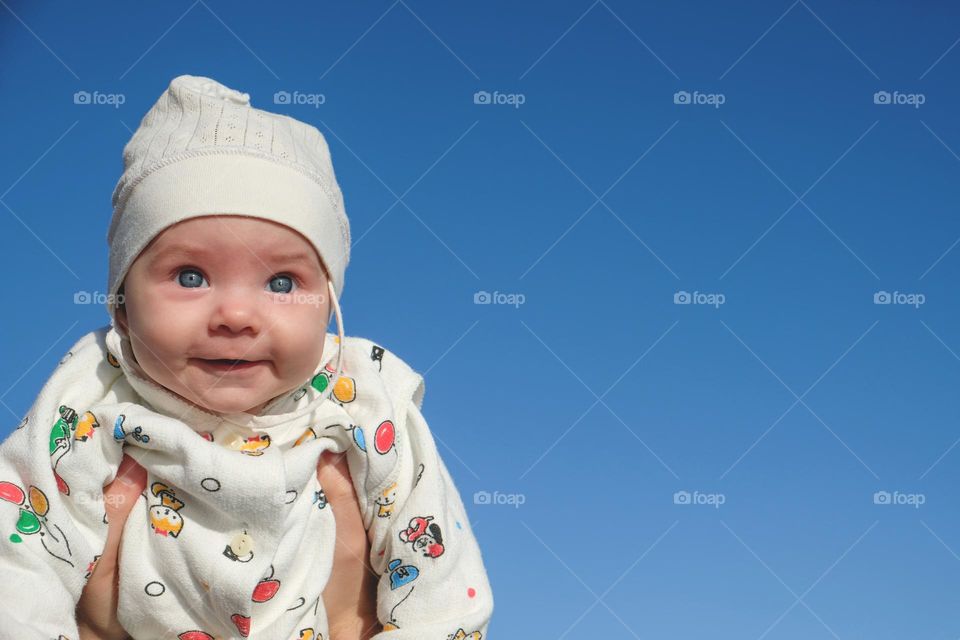 Smiling and surprised baby against the blue sky