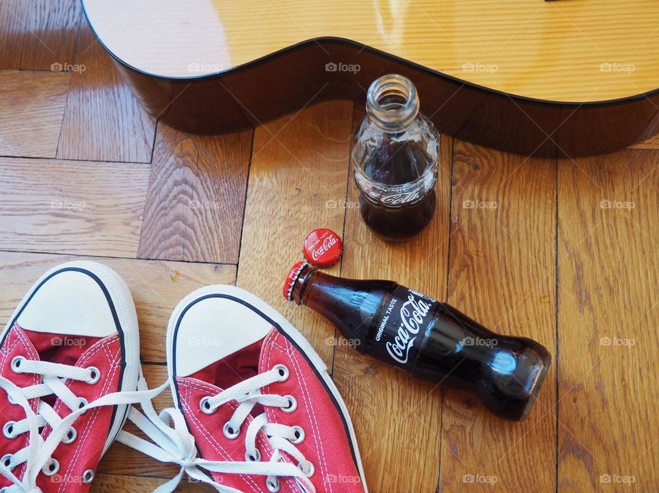 Coca Cola bottles on hardwood floor with red sneakers and a guitar.