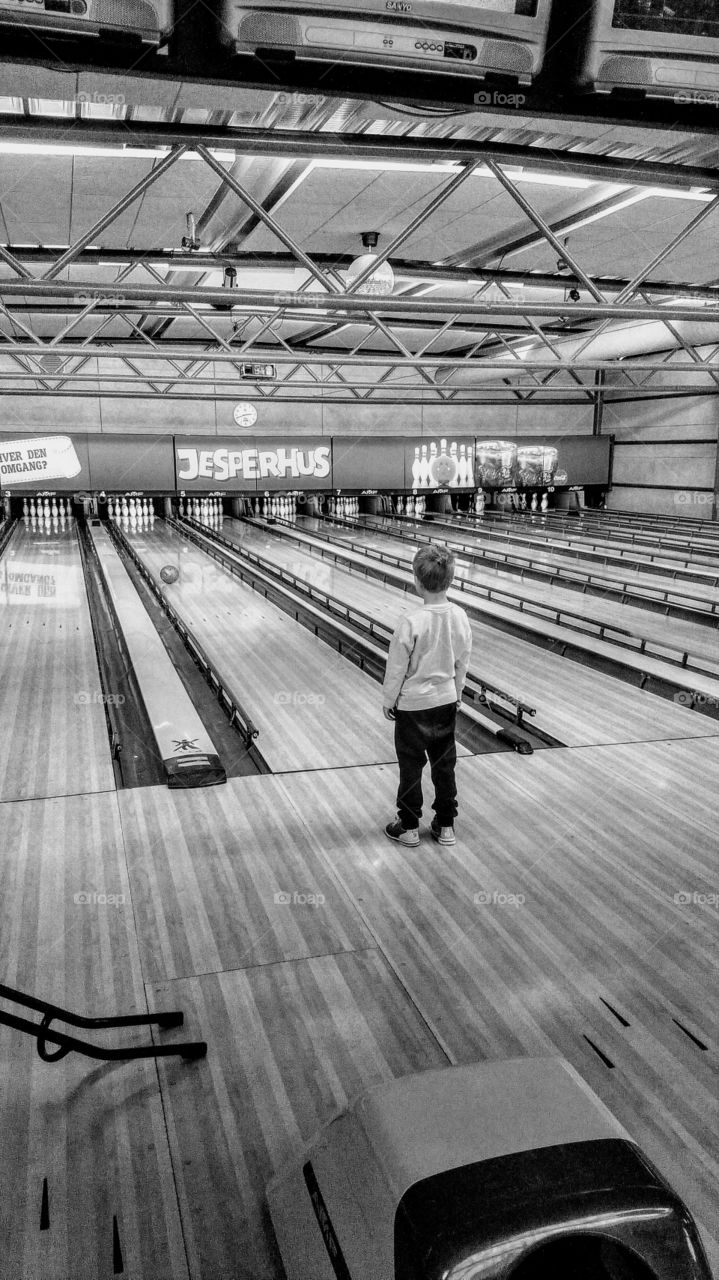 Kid bowling, watching the bowling ball running down the lane. In a entertainment center in Denmark on holiday.