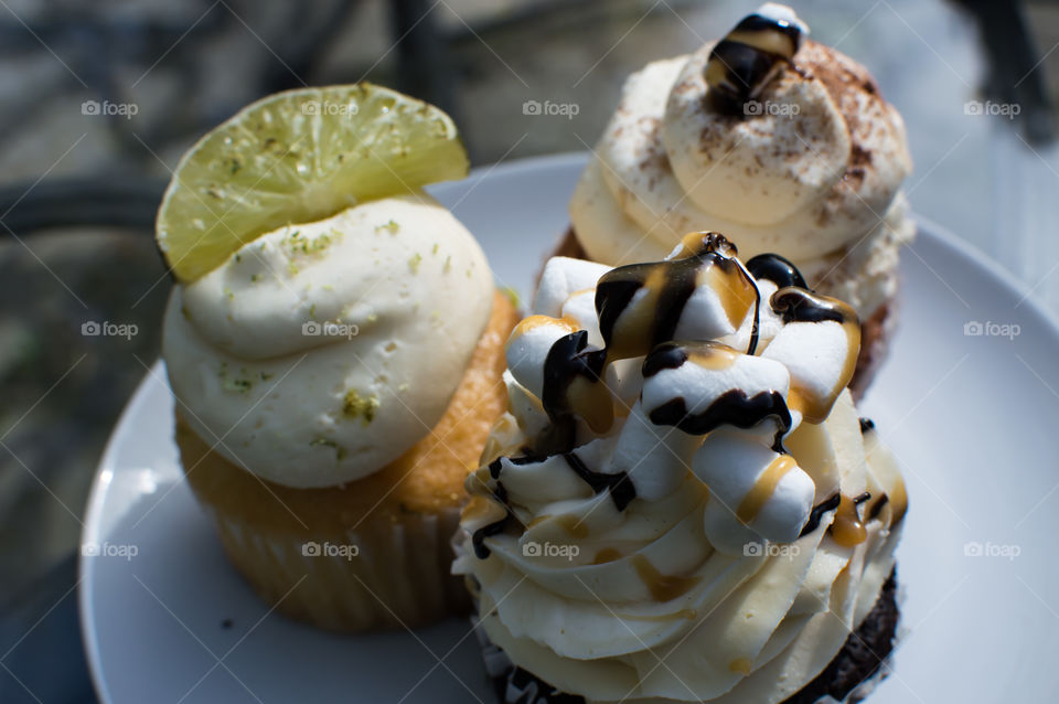 Trip of beautiful cupcakes on patio table for coffee time or afternoon tea party fresh lime and citrus spice cupcake and rocky road chocolate and caramel marshmellow decorated frosting