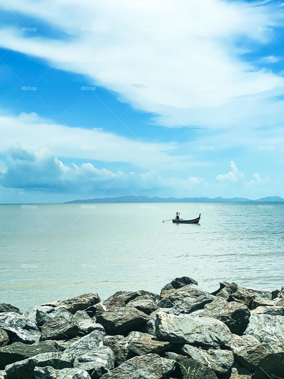 A fisherman on a boat in a clam sea with cloudy sky background 