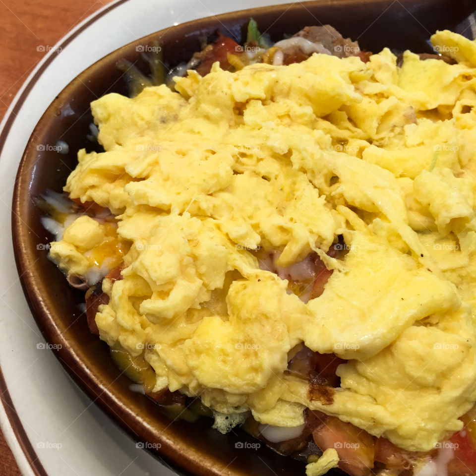 Square photo of breakfast meal. Skillet fillet with meats, veggies and topped with scrambled eggs. 