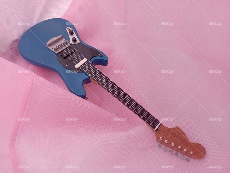 Blue miniature guitar inside pink shoping bag.