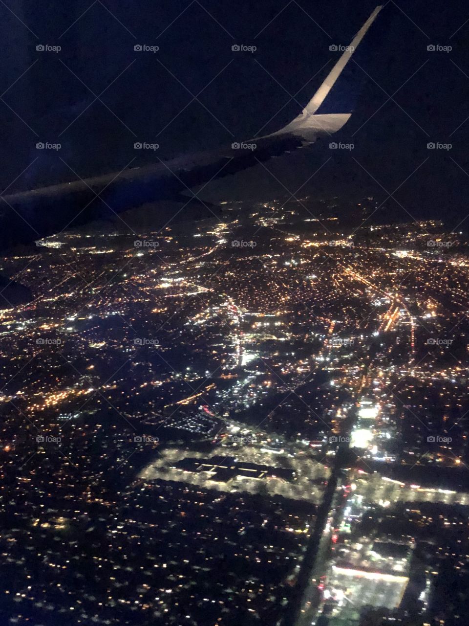A picture of an illuminated city scape taken from the window of an airplane on an evening flight. 
