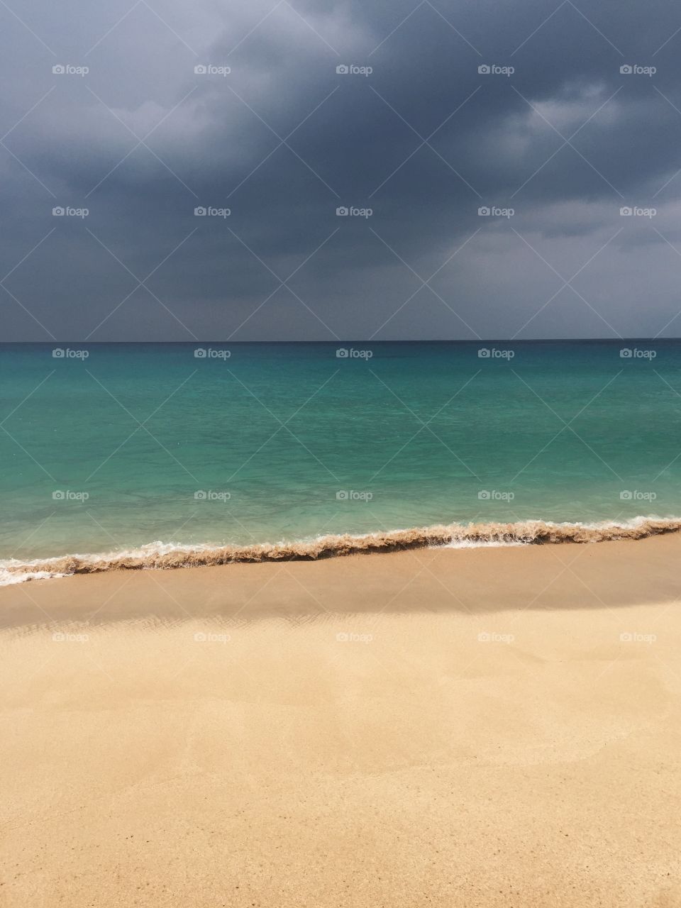 Stormy skies hang over crystal clear blue water on a beach on the north shore of Oahu, Hawaii.