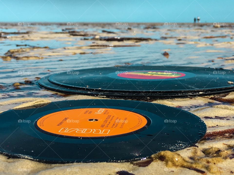 Turquoise sky and water, vintage record vinyl LP in ocean washed up on shore low tide sandy beach