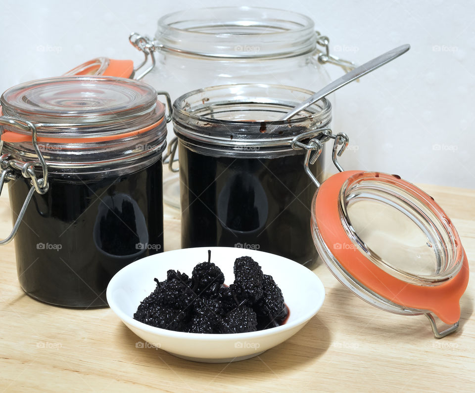 Fresh mulberries in syrup in a small white dish with two full jars and a spoon.