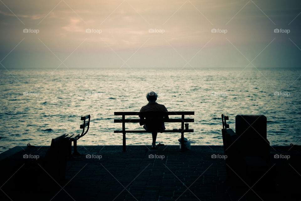 Man Silhouette Sitting On A Bench In Front Of The Sea On Sunset And Reading A Book
