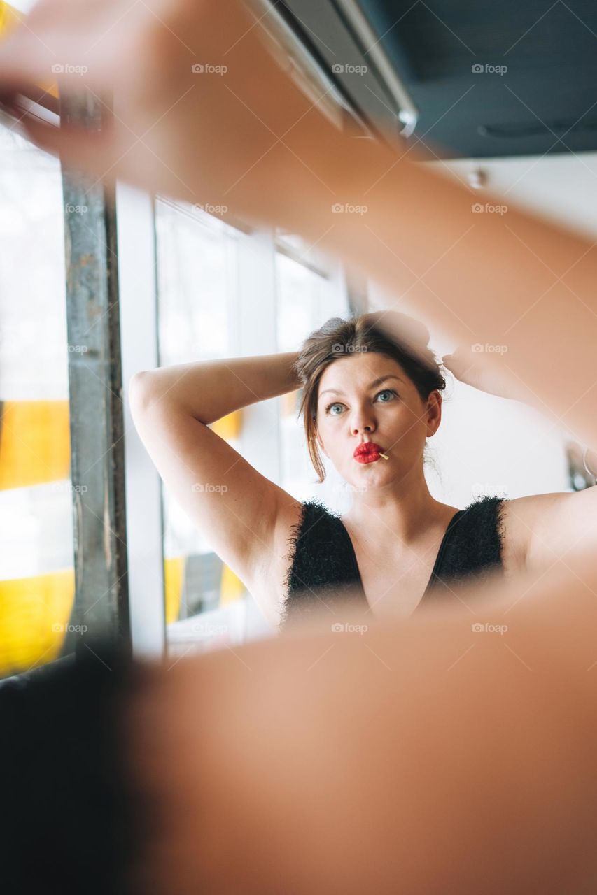 Beautiful smiling young woman plus size body positive in black evening dress make hair style near mirror at beauty studio