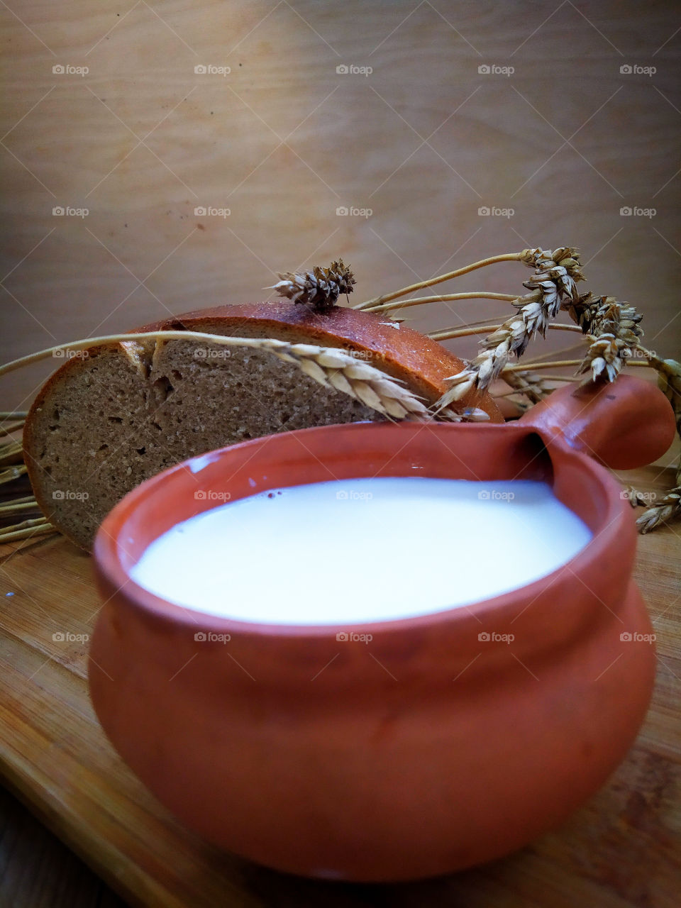 Still life: a clay mug with milk, a piece of bread and ears of wheat