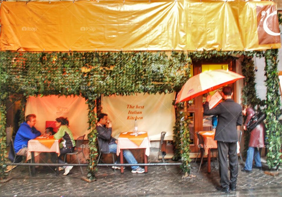 Rainy Roman cafe. A man with an umbrella waits for a table at an outdoor cafe in Rome