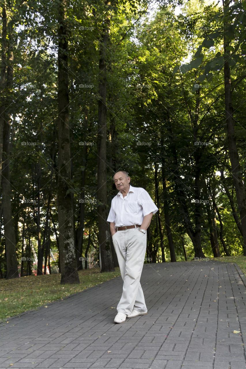 A lonely pensioner in a white shirt and white pants walks in the park.