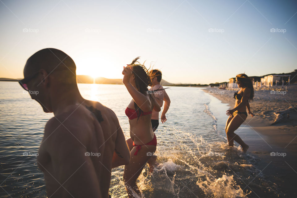 group of friends having fun at the beach in summertime during sunset