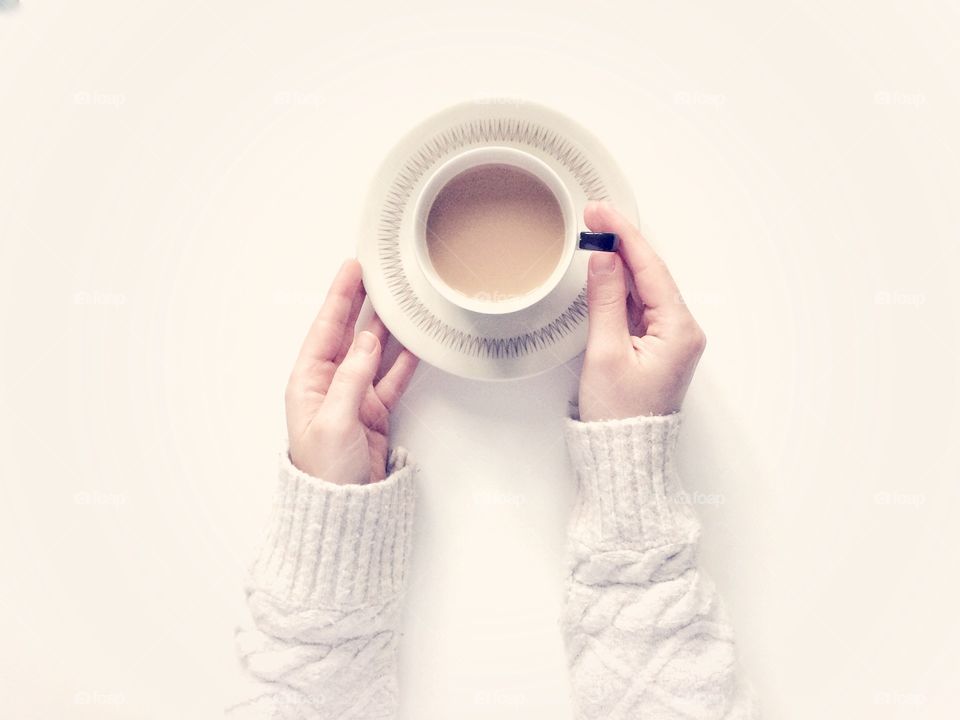 Looking Down from above onto a white background with a girl in a cosy sweater holding a cup of tea in a cup and saucer 