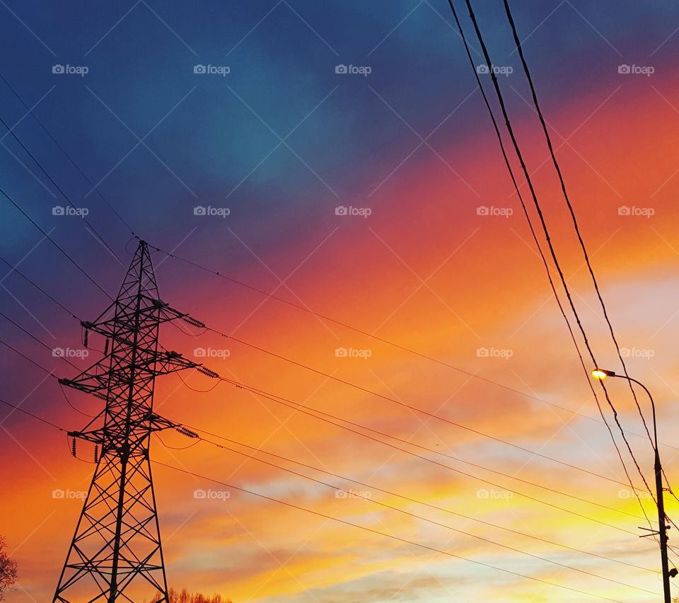 Electricity pylon with illuminated street light at sunset