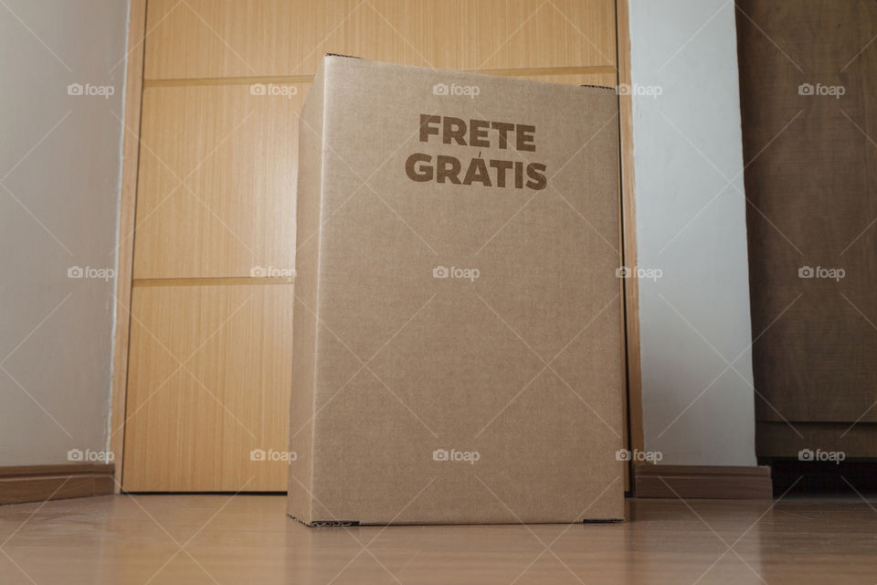 Detail of man with black gloves holding a cardboard box written free shipping to deliver products on gray background. Delivery concept. Delivery service concept. Copy space. Black friday concept.