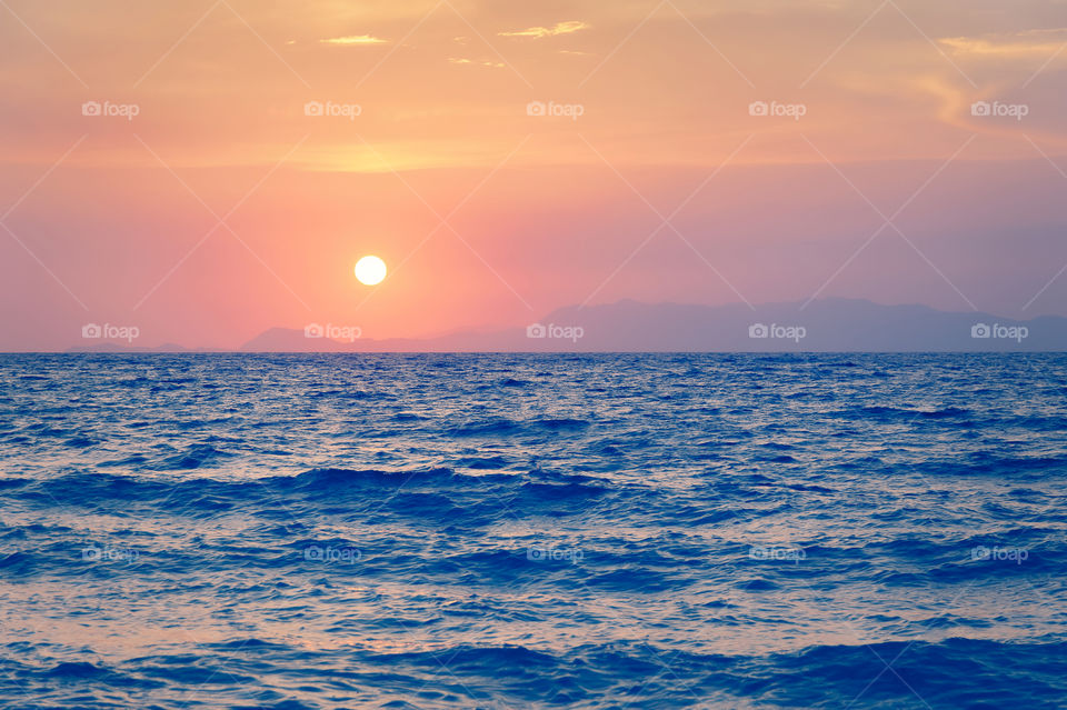 Sunset over Aegean sea in Mediterranean. Low sun lit tiny contour of Turkish coastline. Island of Rhodes. Greece. Europe.