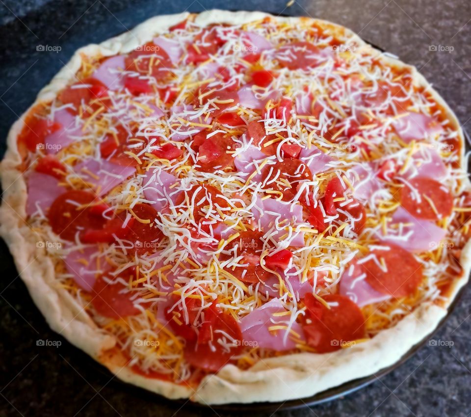 Closeup of a homemade pepperoni and Canadian bacon pizza with lots of cheese ready to be baked. 