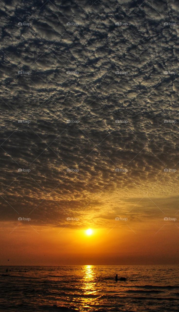 An orange sly, a sunset from the beach, with so many fluffy clouds above and some sea waves near.