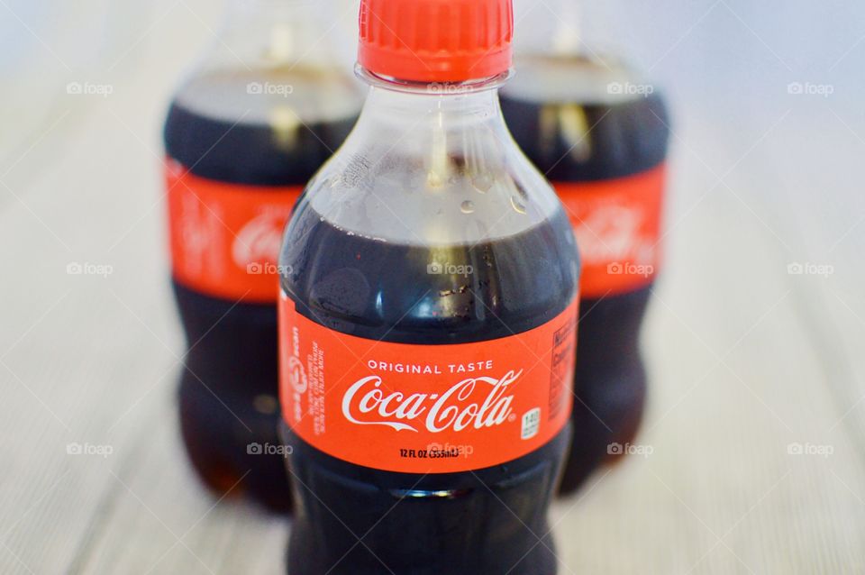 Three plastic bottles of Coca-Cola on a white rustic background