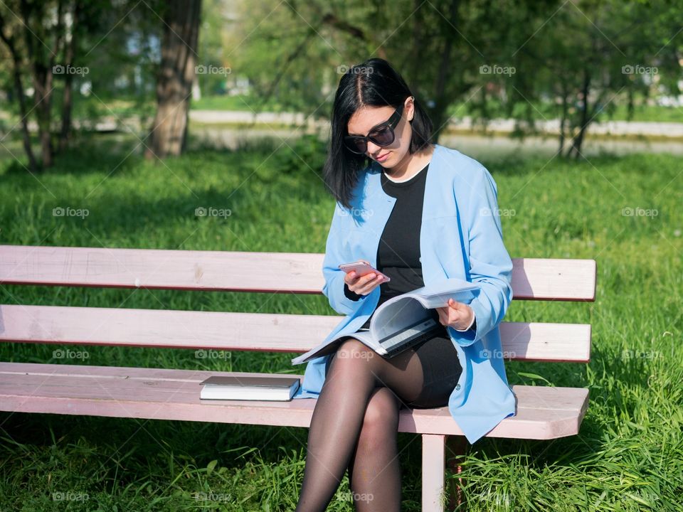 Business woman using her smartphone while sitting on the park bench 