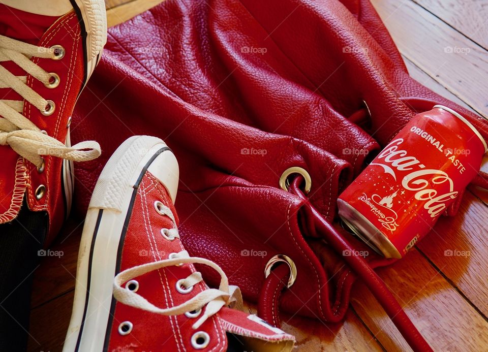 Can of Coca Cola next to red bag and sneakers on hardwood floor.